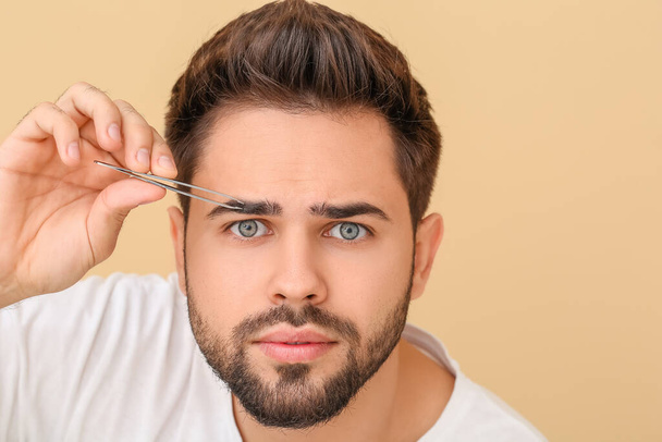 Young man correcting eyebrow shape on color background - Foto, immagini