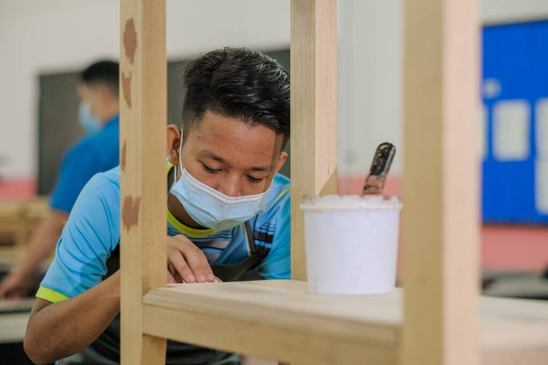 Giovane falegname in abiti da lavoro e maschera facciale utilizzando riempitivo in legno nel lavoro di finitura per consolle . - Foto, immagini