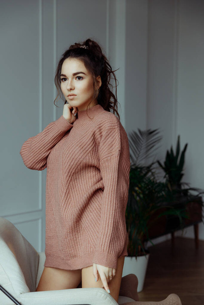 Young brunette woman with gathered hair looks to the side. The woman is wearing a pink knit sweater. High quality photo - Photo, Image