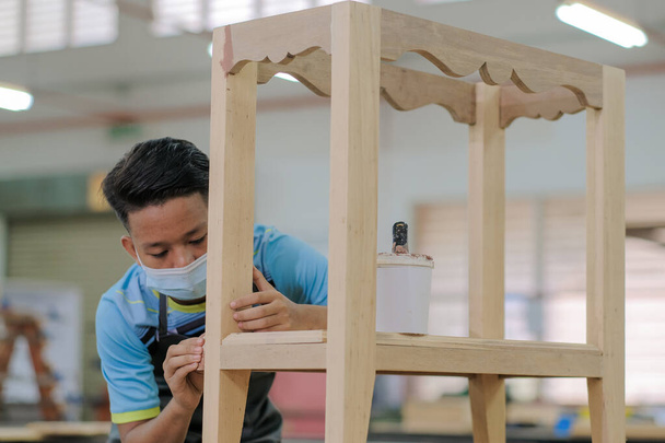 Молодой плотник в рабочей одежде и маске для лица с использованием деревянного наполнителя для отделочных работ для консольного стола . - Фото, изображение