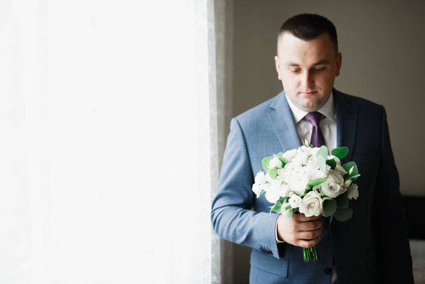 Beautiful man, groom holding big and beautiful wedding bouquet with flowers - Zdjęcie, obraz