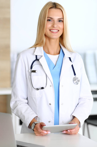 Doctor woman at work in hospital excited and happy of her profession. Blonde physician controls medication history records and exam results while using tablet computer. Medicine and healthcare concept - Foto, Imagem