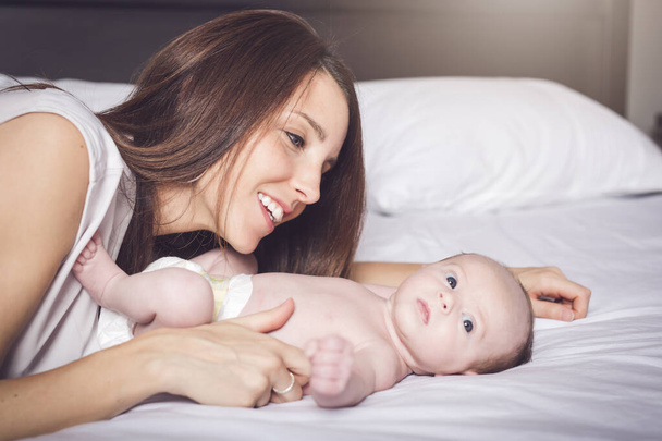 A happy mother with baby on bed - Фото, изображение
