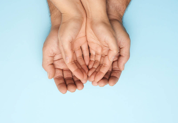 Dwie kobiece dłonie leżą w męskich dłoniach na niebieskim tle, widok z góry. Koncepcja rodziny - Zdjęcie, obraz