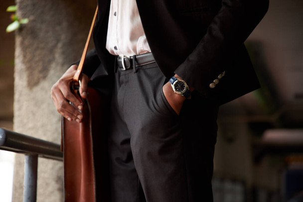 Κοντινό πλάνο του επιχειρηματία με δερμάτινη τσάντα στέκεται με το χέρι στην τσέπη - Φωτογραφία, εικόνα
