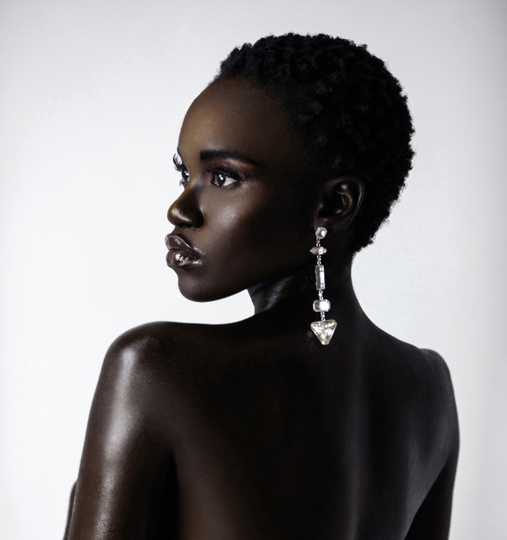 Um retrato de uma jovem mulher negra sexy com cabelo preto curto e batom úmido vestindo um grande brinco de diamante na frente de um fundo brilhante. - Foto, Imagem