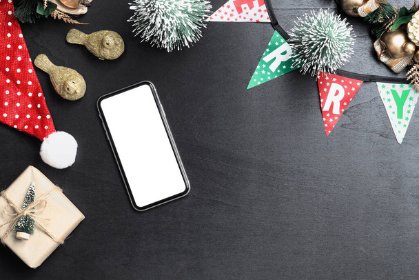 Mockup blanco witte scherm smartphone op zwart bureau tafel achtergrond voor Kerstmis en Nieuwjaar feest achtergrond, Flat lay bovenaanzicht met kopieerruimte voor uw Vrolijk Kerstfeest en Gelukkig Nieuwjaar kunstwerk. - Foto, afbeelding