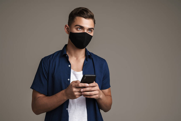 Image of caucasian guy in face mask using mobile phone isolated over grey background - Φωτογραφία, εικόνα