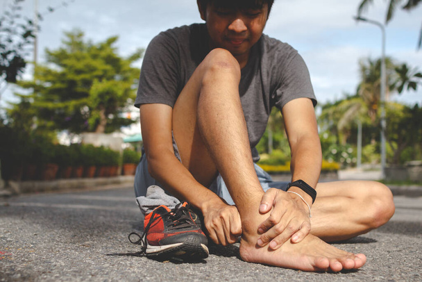 Sport man holding ankle in pain due to sprained ankle.Injury from workout concept. - 写真・画像
