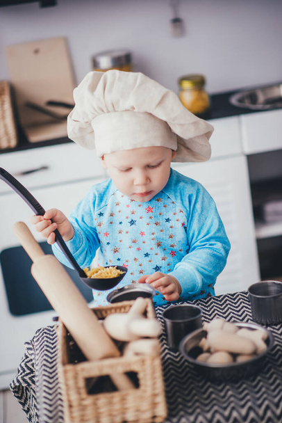 Gyerek fiú séf kalapban és merőkanál a konyhában - Fotó, kép