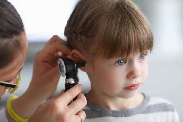 Otorhinolaryngologist examines little girls ear with otoscope in clinic - Photo, Image
