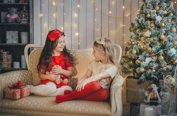 Two young girls exchange gifts against the background of a decorated christmas tree - Photo, Image