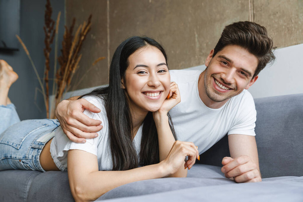 Beautiful young happy couple laying on couch, embracing - Фото, зображення