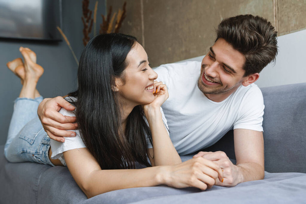 Beautiful young happy couple laying on couch, embracing - Fotografie, Obrázek