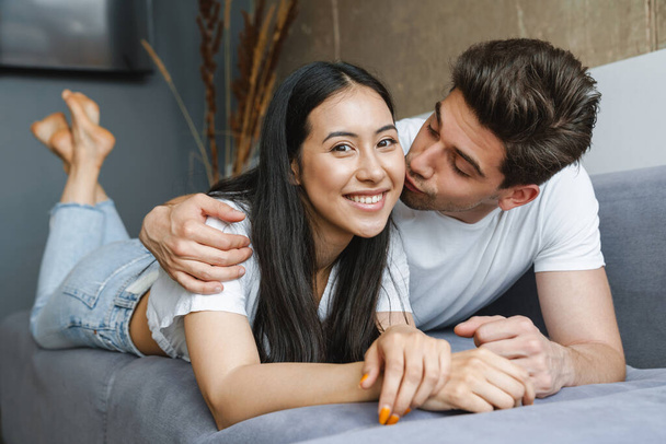 Beautiful young happy couple laying on couch, embracing - 写真・画像