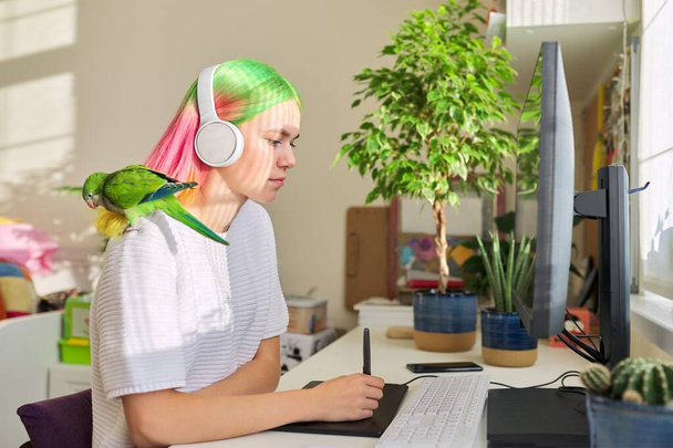 Kulaklıklı öğrenci kız bilgisayarda papağanla, grafik tabletle çalışıyor. - Fotoğraf, Görsel