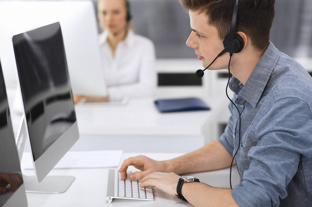 Call center. Group of casual dressed operators at work. Focus on young businessman in headset at customer service office. Telesales in business - Foto, Imagen