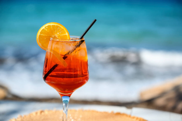 Červený koktejl s pomerančovým plátkem a ledem na mořském pozadí - Fotografie, Obrázek
