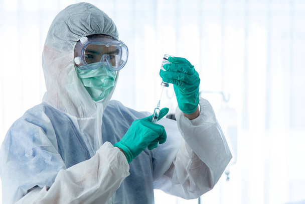 A védőruhás orvosok ellenőrzik és injekciózzák a CORONA VISRUS-szal vagy COVID-19-cel fertőzött beteget a kórház karanténszobájában.. - Fotó, kép