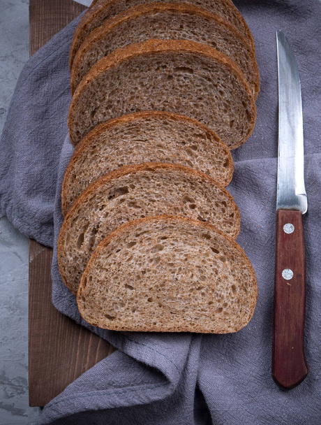 Sliced homemade white black wheat bread with wheat flour on old wood tray on grey background. Top view - Photo, Image