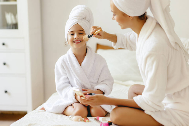 happy family mother and little daughter in dressing gowns and towels laugh and do makeup  a Spa day at hom - Foto, imagen
