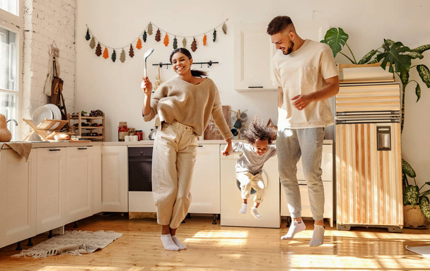 Happy family: full body delighted diverse parents playing and dancing with son in cozy kitchen on weekend day at hom - Φωτογραφία, εικόνα