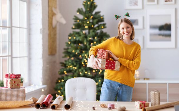 Счастливая молодая женщина с упакованными подарками на Рождество улыбается в камеру у хома - Фото, изображение