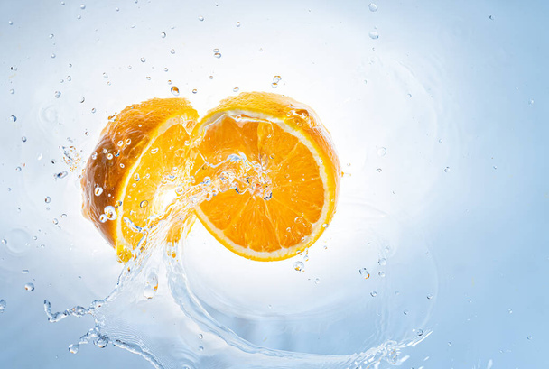 Zwei Hälften orangefarbener Früchte spritzen ins klare Wasser. - Foto, Bild