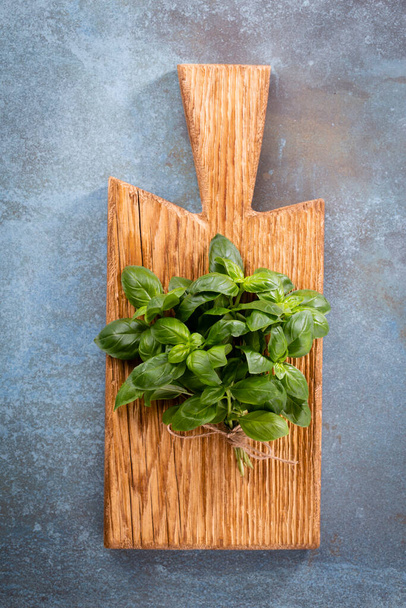 Bunch of fresh organic basil in cutting board on rustic wooden background - Photo, image