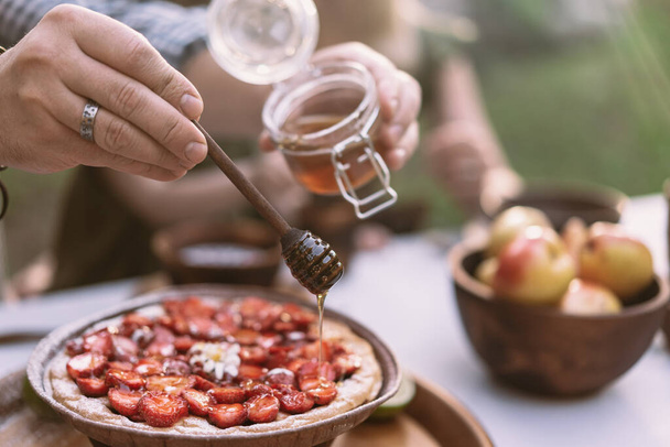 Hand pouring honey on strawberry pie - Zdjęcie, obraz