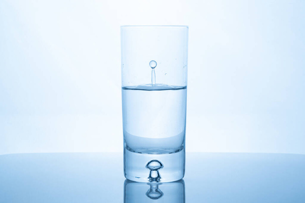 Water drop splash inside glass half full against bright background. Purity and health concept - Foto, Imagem