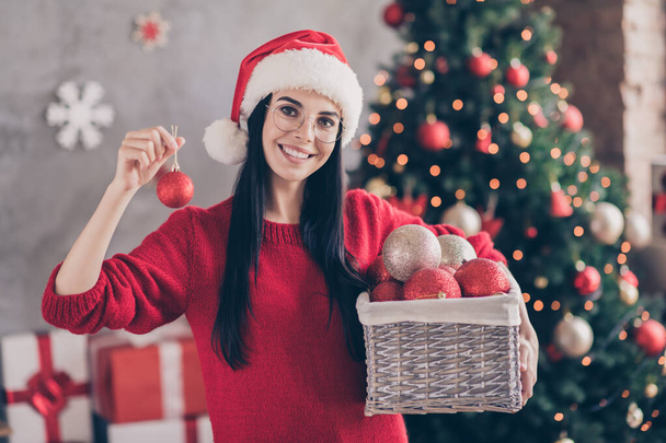 Photo of positive girl wear santa claus headwear hold christmas balls box in house indoors with x-mas spirit ornament - Fotó, kép