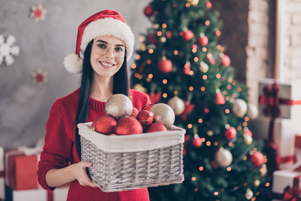 Photo of girl in santa claus cap hold christmas baubles tinsels box in house indoors with x-mas lights garlands ornament - Foto, Imagen