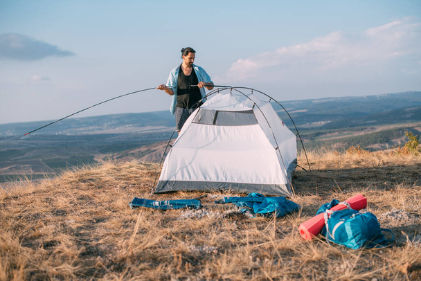Junge männliche Touristen schlagen ein Zelt in den Bergen auf. Der Mann schlägt bei einer Wanderung sein Lager auf, sammelt bei Sonnenuntergang allein ein Zelt in den Bergen - Foto, Bild