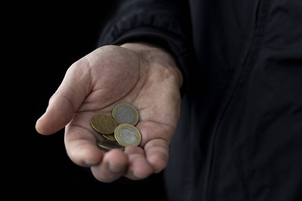 Νομίσματα ευρώ σε ανδρικό χέρι σε μαύρο φόντο. Η έννοια της χρηματοπιστωτικής κρίσης και της φτώχειας στην ΕΕ. - Φωτογραφία, εικόνα