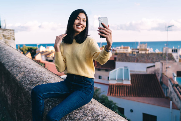 Happy Asian traveller clicking selfie images with overlooking scenery on background, cheerful millennial blogger shooting influence vlog during summer vacations for visiting touristic places - Photo, Image