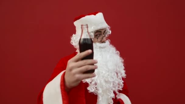 Glücklicher Weihnachtsmann trinkt Cola auf rotem Grund, blickt lächelnd in die Kamera und zeigt den Daumen in die Kamera. - Filmmaterial, Video