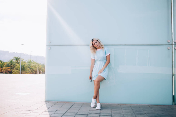 Full length portrait of young female model in casual sundress posing near urban wall during fashion photo session, Caucasian hipster girl 20 years old dressed in trendy clothing looking at camera - Valokuva, kuva