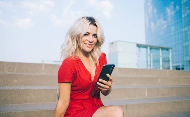 Portrait of happy Caucasian travel blogger resting at urban stairs enjoying free time for online networking via modern cellular device, millennial woman with digital smartphone smiling at camera - Foto, immagini