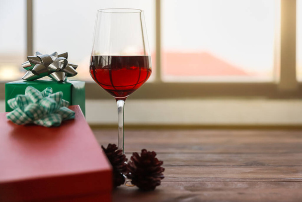 New Year, Christmas and Holiday Season Concept. Closeup of red wine glass with beautiful red and green gift box on old wooden plank with copy space. - Foto, Imagem
