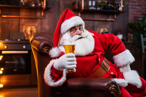 Santa Claus drinks beer while sitting in a leather armchair - Foto, Imagem