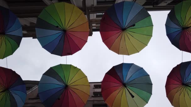 Veel kleurrijke regenboog open paraplu 's hangen over smalle straat tussen huizen. - Video