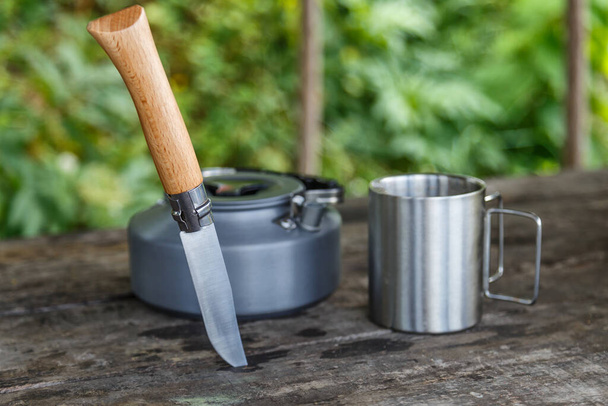 Kettle with a mug in a tourist camp. outdoor recreation in the Carpathian forest. knife and a mug on a wooden stand in outdoor. Tourist - 写真・画像