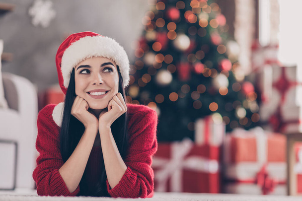 Photo of lovely young girl lay floor hands face chin beaming smile look up wear santa cap red pullover in decorated living room indoors - Photo, Image
