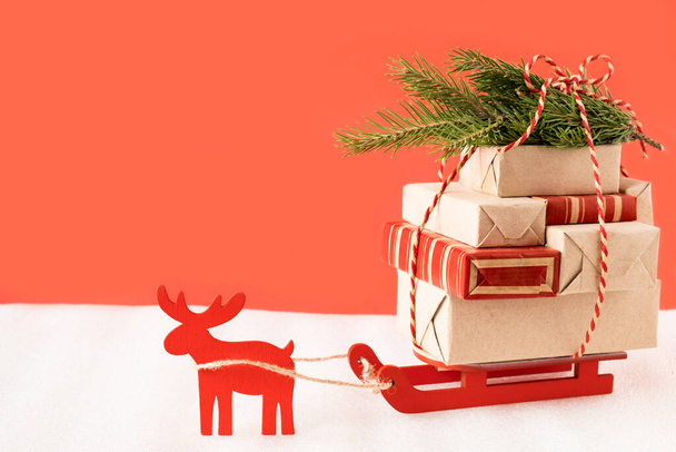 Toy reindeer and sleigh delivering christmas gifts and tree on festive red background - Foto, imagen