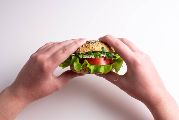 Female hands holding veggie burger with tomatoes, cheese, lettuce and microgreens, white background, close up. - Foto, Bild