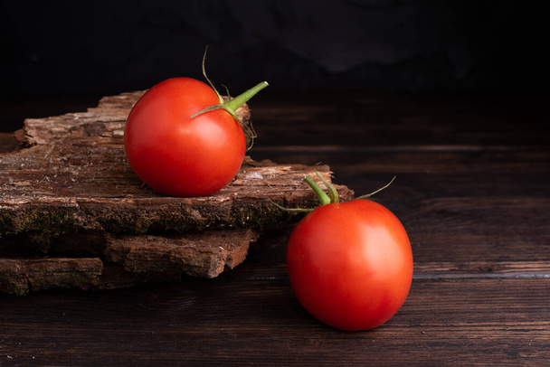 Δύο κόκκινες φρέσκες ντομάτες σε ξύλινο τραπέζι και σκούρο ξύλινο φόντο. - Φωτογραφία, εικόνα