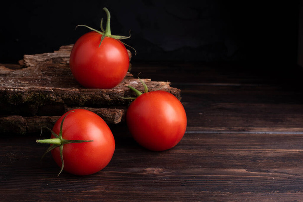 Τρεις κόκκινες φρέσκες ντομάτες σε ξύλινο τραπέζι και σκούρο φόντο. - Φωτογραφία, εικόνα