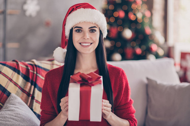 Photo of pretty young lady sit couch hold present wear santa headwear red pullover in decorated living room indoors - Foto, immagini