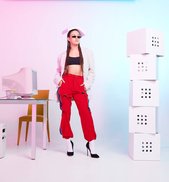 Stylish female office worker with obsolete computer and paper on head posing on workplace. Colored Neon light - Фото, зображення